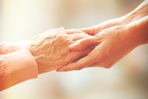 Care assistance A person holds the hands of an elderly person