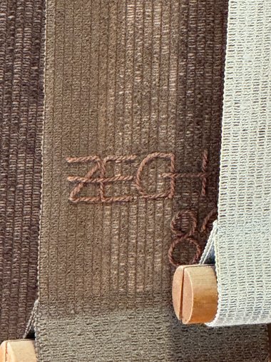 Brown embroidery of the letters "ZECH" on a brown fabric panel.