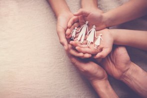 several hands on top of each other holding a garland consisting of a family made of paper
