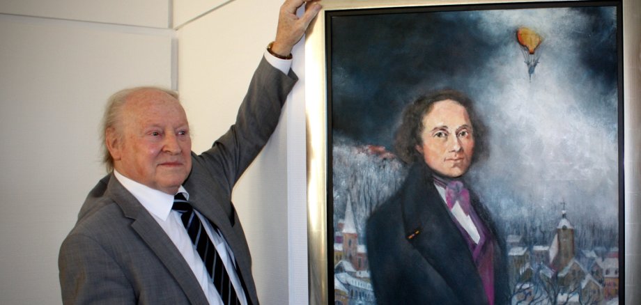 Hermann Theophil Juncker avec son portrait de Johann Georg August Wirth, qui vivait à Hombourg en 1832 à la veille de la fête de Hambach et y publiait son journal "Deutsche Tribüne". Juncker a réalisé ce tableau en 2009 pour la ville de Hombourg. Photo : Martin Baus Hermann Theophil Juncker avec son portrait de Johann Georg August Wirth, qui vivait à Hombourg en 1832 à la veille de la fête de Hambach et y publiait son journal "Deutsche Tribüne". Juncker a réalisé ce tableau en 2009 pour la ville de Hombourg. Photo : Martin Baus