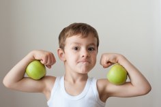 Un garçon qui présente deux pommes sur ses biceps