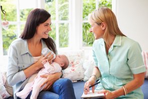 Une femme tient un bébé dans ses bras et est assise à côté d'une autre femme qui la conseille.