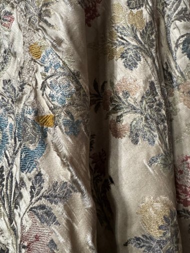 Abito da sposa Maria Amalie Foto a colori di un tessuto luccicante con due pieghe piuttosto ampie. Su di esso sono ricamati diversi motivi floreali.