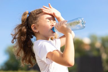 Bambina che beve acqua da una bottiglia sotto il sole cocente. Bambina che soffre Bambina che beve acqua da una bottiglia sotto il sole cocente. Bambina che soffre