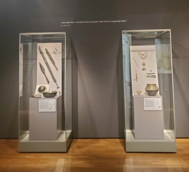 Показывает Merovingian SB Цветная фотография двух витрин с мечом и наконечником копья слева и золотыми украшениями справа.