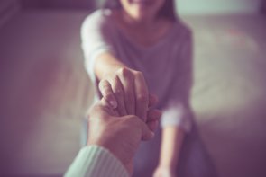 Sonstige Hilfen sitzende Frau hält die Hand von einer stehenden Person