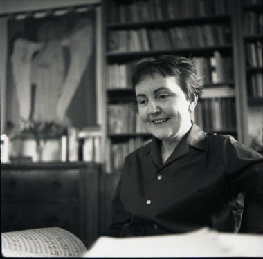 Erna Woll 1967 Schwarz-Weiß Foto einer lächelnden Frau mit kurzen Haaren an einem Schreibtisch vor einem Bücherregal.