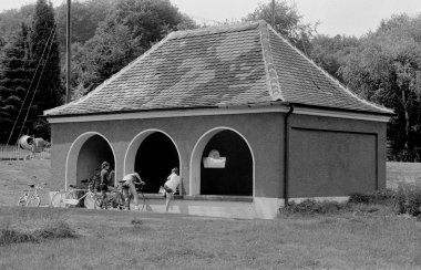 Schwarz-Weiß-Foto eines überdachten Waschhauses, vor welchem mehrere Kinder mit ihren Fahrrädern geparkt haben.