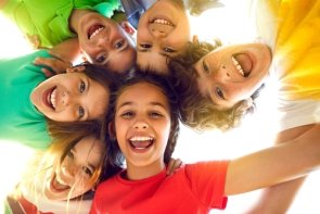 Kinder stehen im Kreis, legen die Arme über die Schultern und lachen