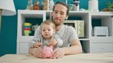 Finanzielle Hilfen Ein Vater hat sein Kind auf dem Schoss und das Kind macht Kleingeld in ein Sparschwein