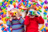 Kindertagesbetreuung Zwei Kinder liegen auf dem Boden und spielen mit bunten Bausteinen