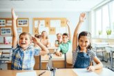  lächelnden Kinder im Klassenzimmer, die ihren Arm heben