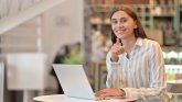 Praktika Frau sitzt am Laptop, zeigt und guckt in die Kamera